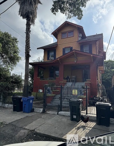 A house with a red and yellow facade is surrounded by a black fence and has a palm tree in front.