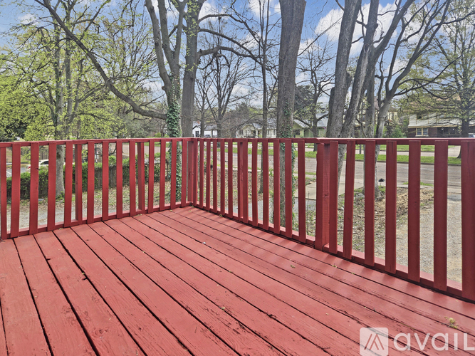 A red wooden deck with a railing and trees in the background.