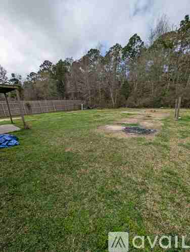 A grassy field with a fence and trees in the background.