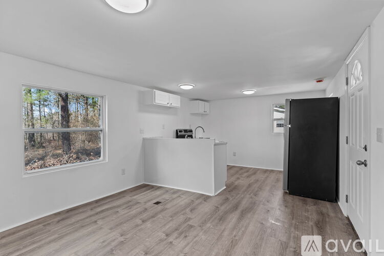 A spacious room with wooden flooring and a large window showing trees outside.