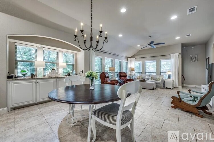 A dining room with a round table and chairs, a chandelier, and a fan.