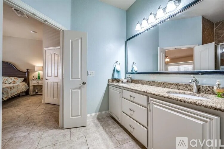 A bathroom with a sink, mirror, and a bedroom with a bed and nightstand.