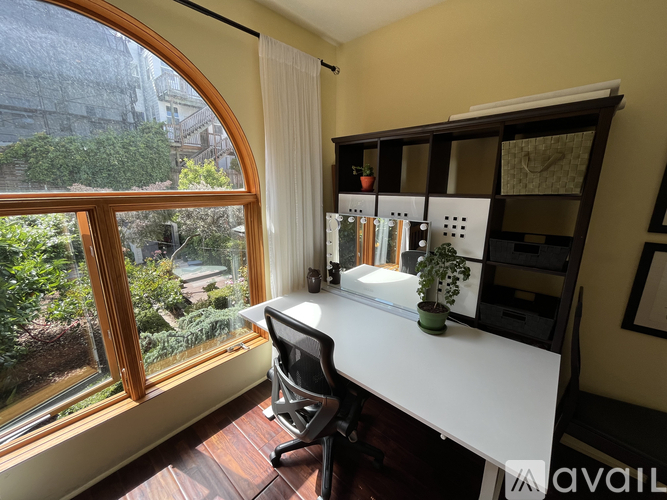 A desk with a computer and a plant on it in front of a window.