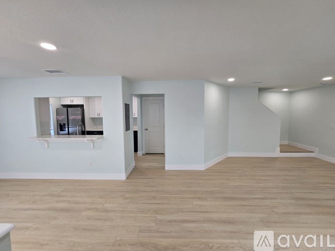 A spacious room with wooden flooring and white walls, featuring a kitchenette with a refrigerator, microwave, and oven.
