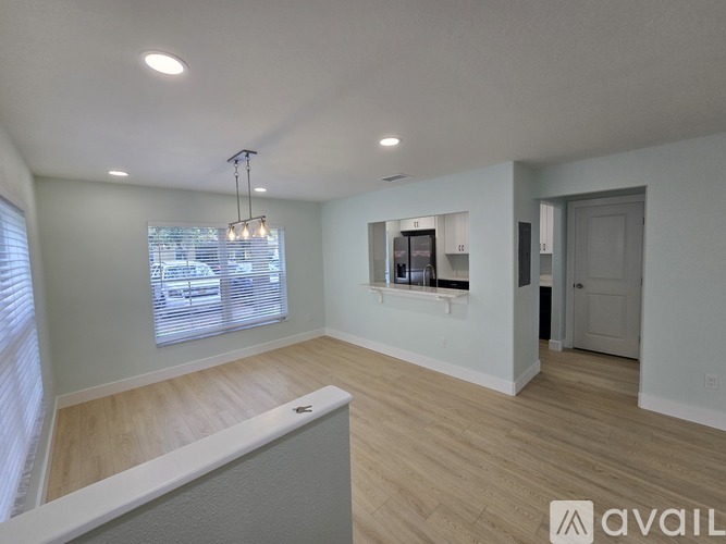 A spacious room with wooden flooring and a large window with blinds.