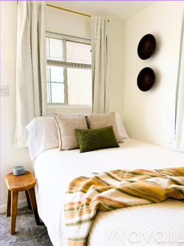 A bedroom with a bed, a blanket, a small stool, and two circular objects on the wall.