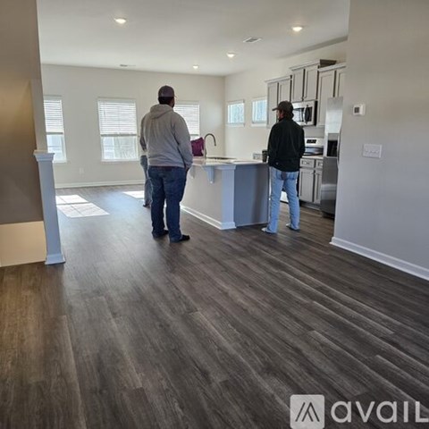 Two men are standing in a kitchen with wooden floors and white walls.