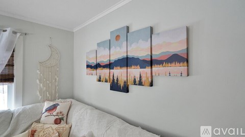 A living room with a couch and a wall with a sunset painting on it.