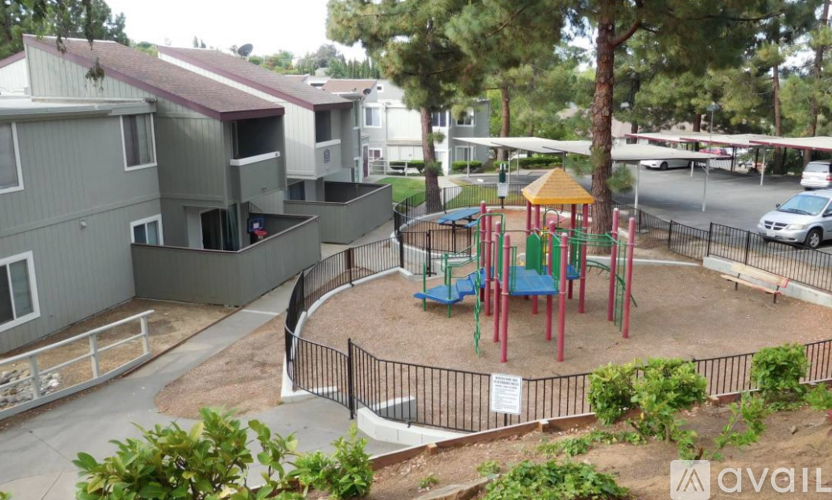 A playground with a swing set and a slide is surrounded by a fence and apartment buildings.