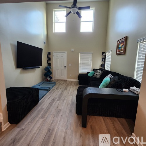 A living room with a black couch and a television mounted on the wall.