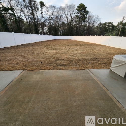 A white fence surrounds a concrete area with dry grass.