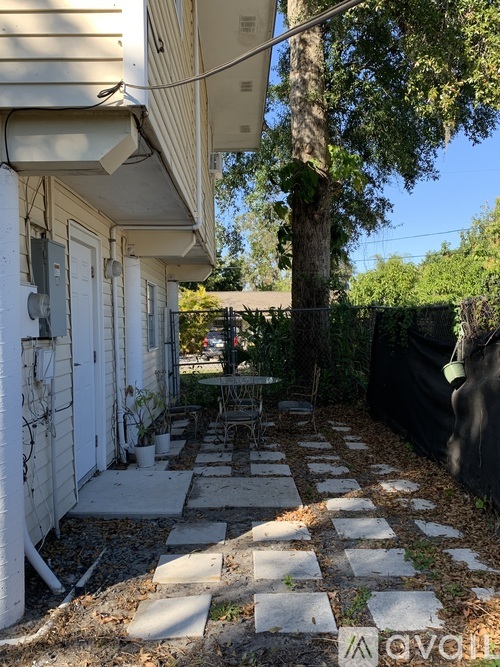 A patio with a table and chairs is surrounded by a white house and a tree.