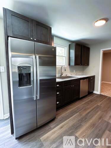 A stainless steel refrigerator in a kitchen with wooden floors.