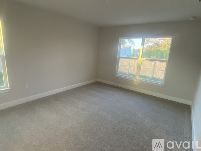 A room with a carpeted floor and a window showing a fence and trees outside.