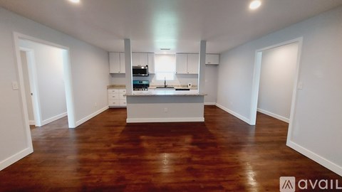 A spacious kitchen with wooden floors and white walls.