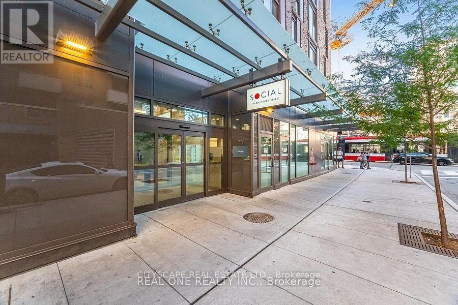 A real estate company's office building with a glass facade and a tree in front.