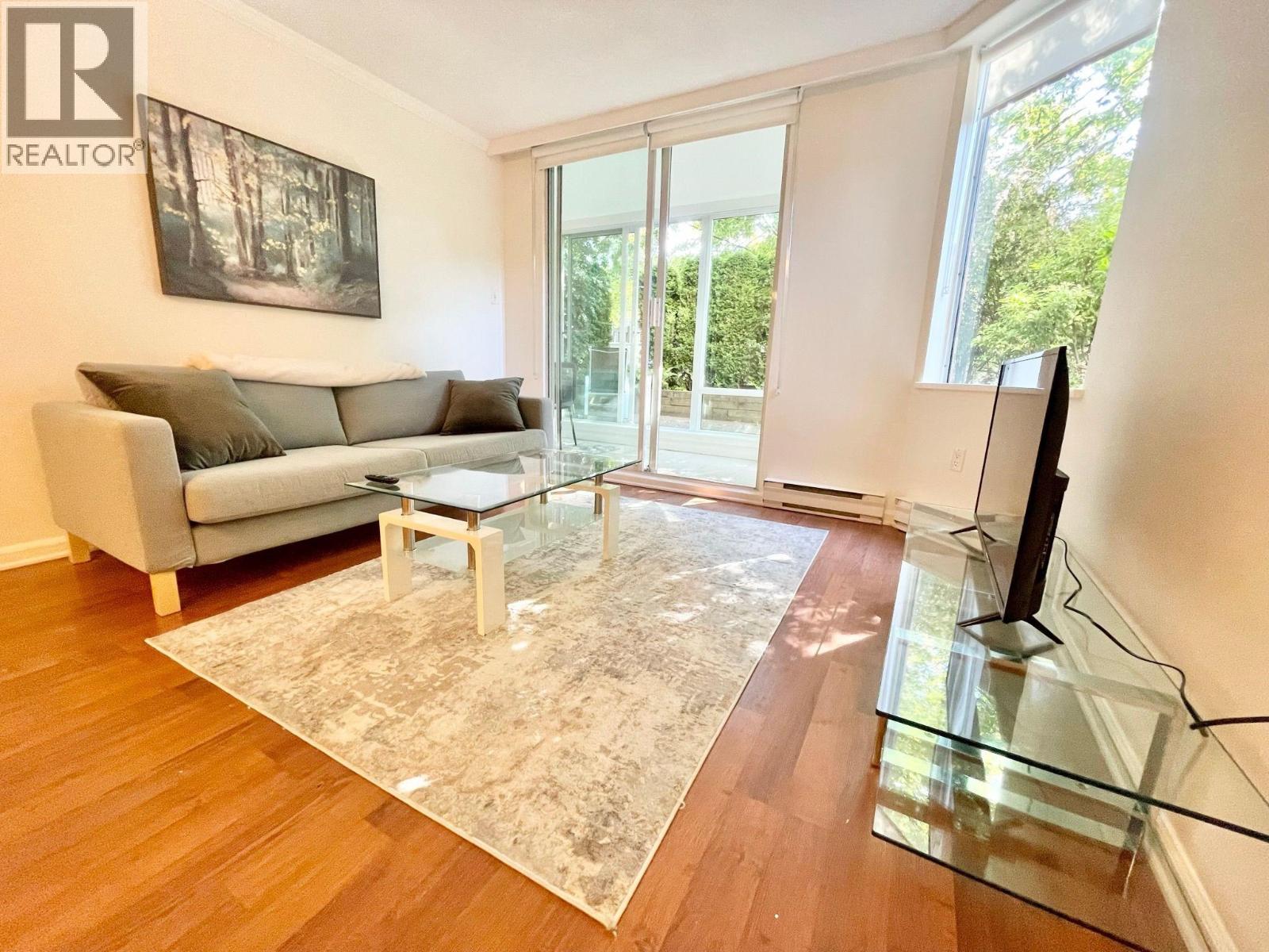 A living room with a grey couch, a glass coffee table, and a painting on the wall.