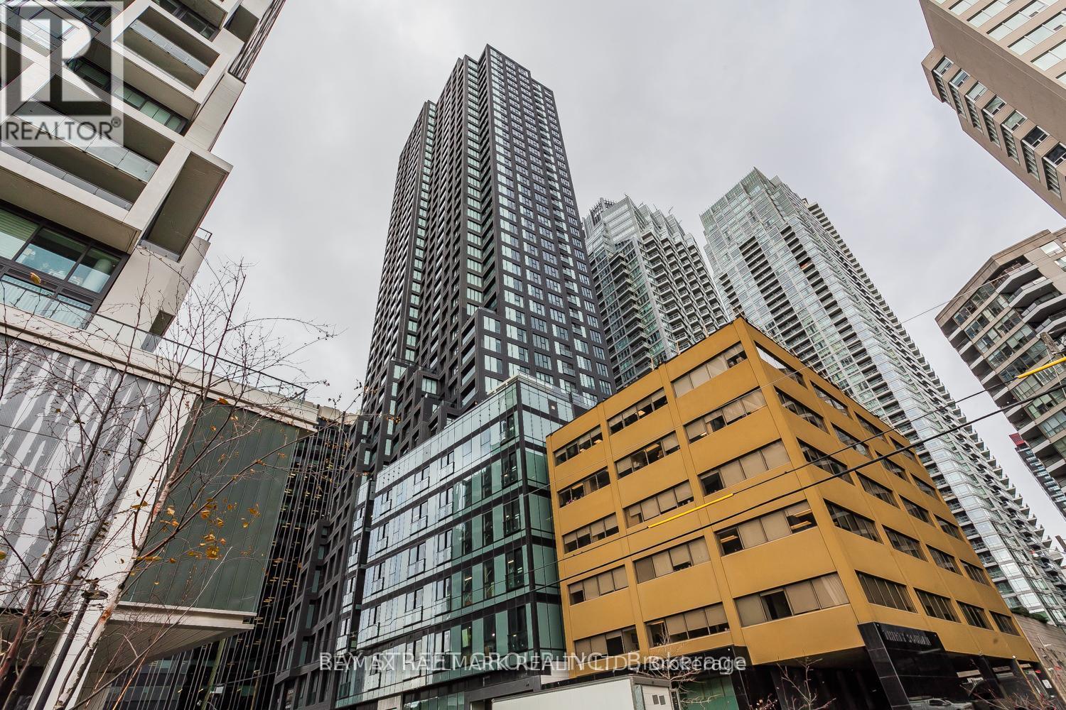 A tall building with a glass facade stands in front of other buildings.