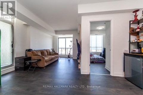 A spacious living room with a brown sofa and a black refrigerator.