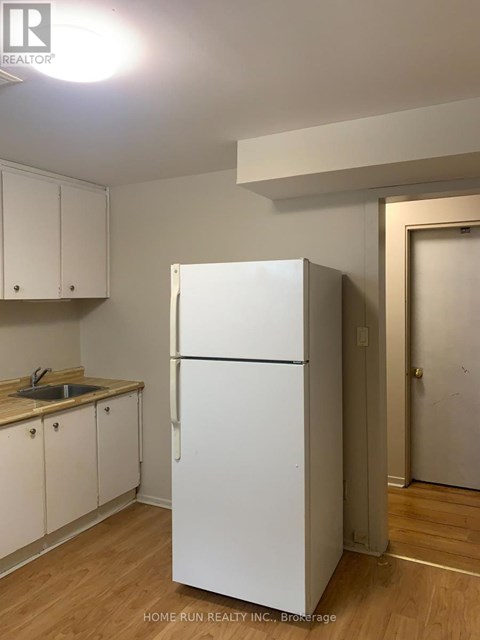 A white refrigerator in a kitchen with wooden floors and white cabinets.