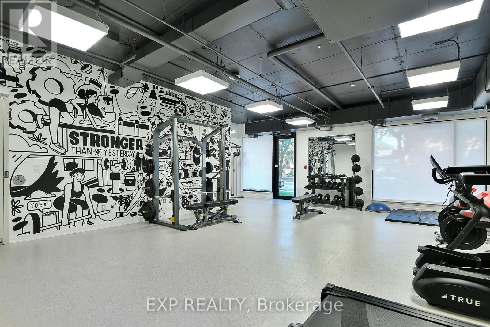 A gym with a wall mural that says "STRONGER THAN YESTERDAY" and exercise equipment.
