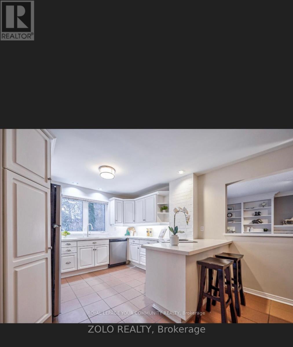 A kitchen with white cabinets and a white island with a bar stool in front of it.