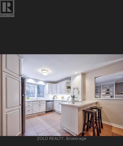 A kitchen with white cabinets and a white island with a bar stool in front of it.