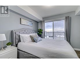 A bedroom with a large bed, a nightstand with a lamp, and a window with a view of the city.