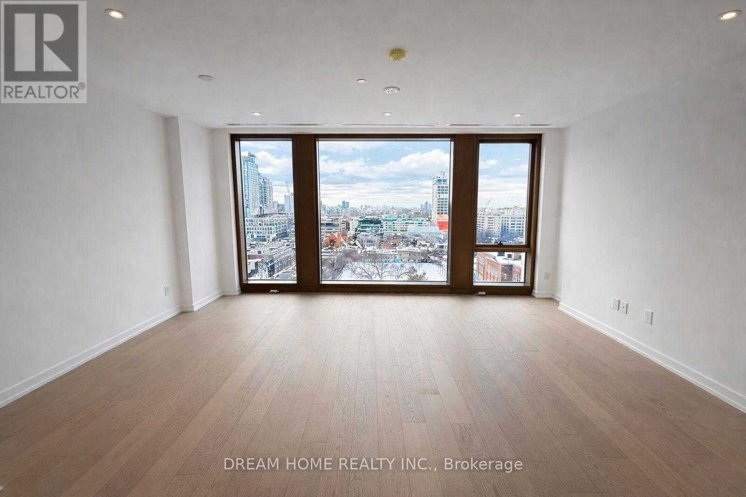 A spacious room with wooden flooring and a large window overlooking a cityscape.