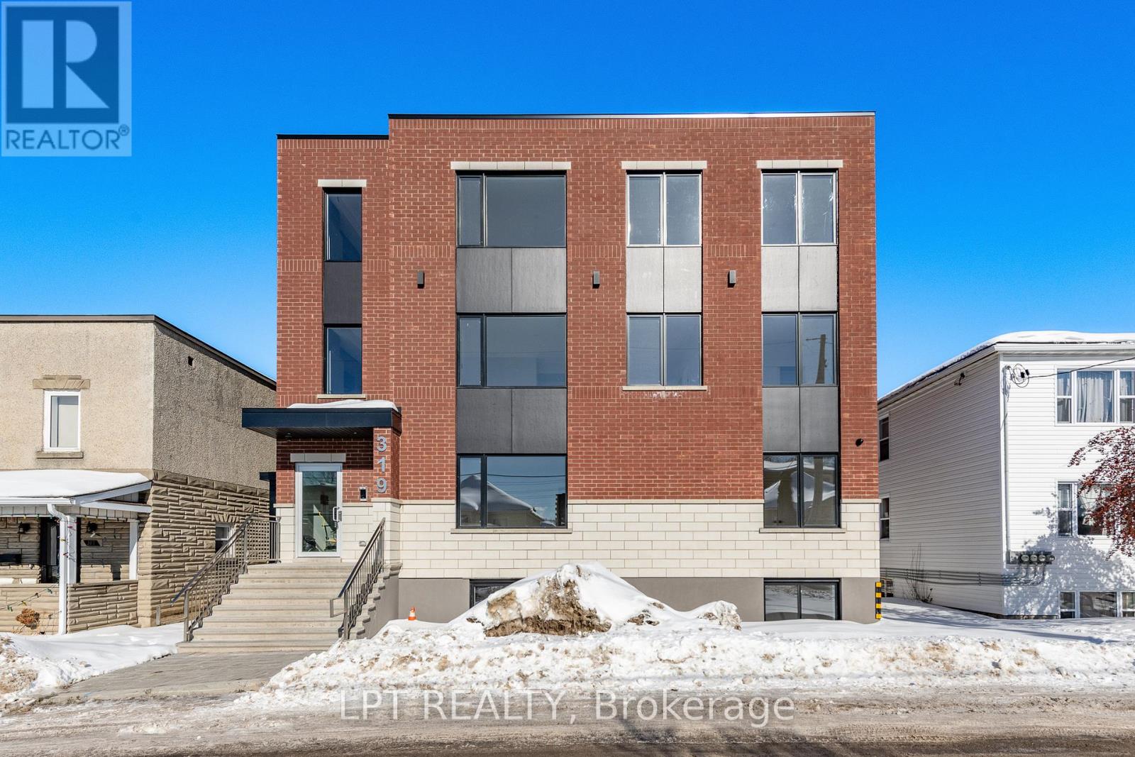 A modern brick building with a glass entrance and a staircase leading to the door.