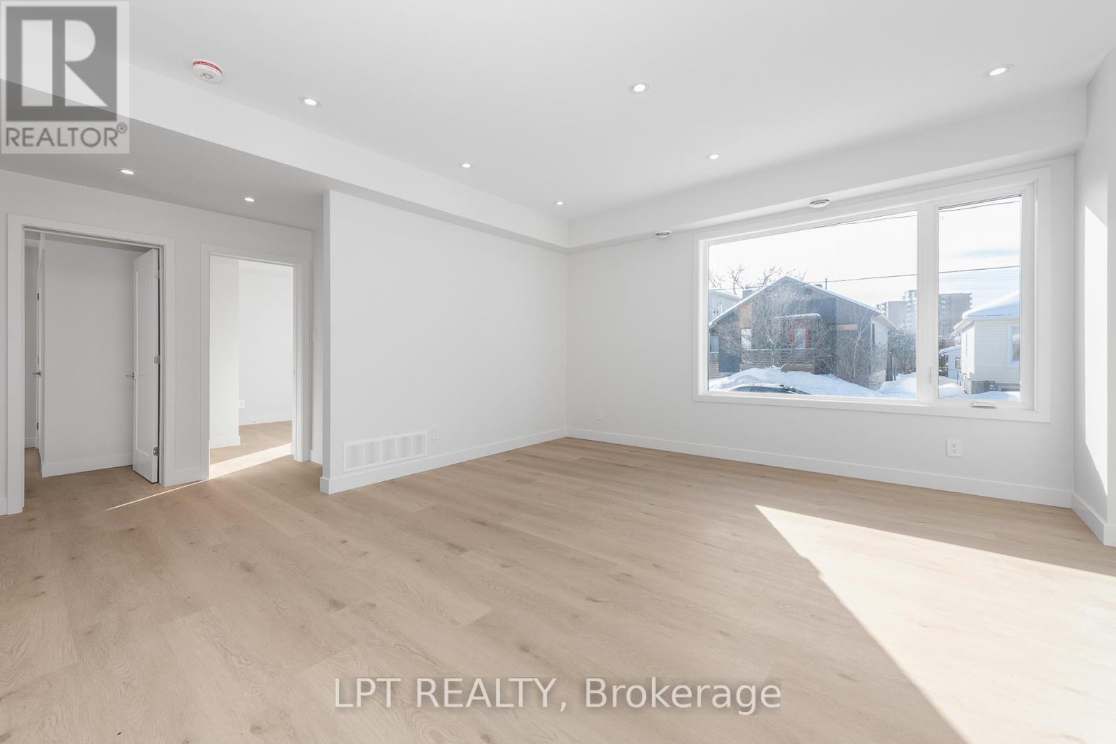 A spacious room with wooden flooring and white walls, with a window showing a snowy landscape outside.