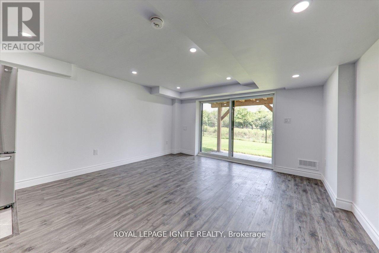 A spacious room with wooden flooring and a sliding glass door leading to a green outdoor area.