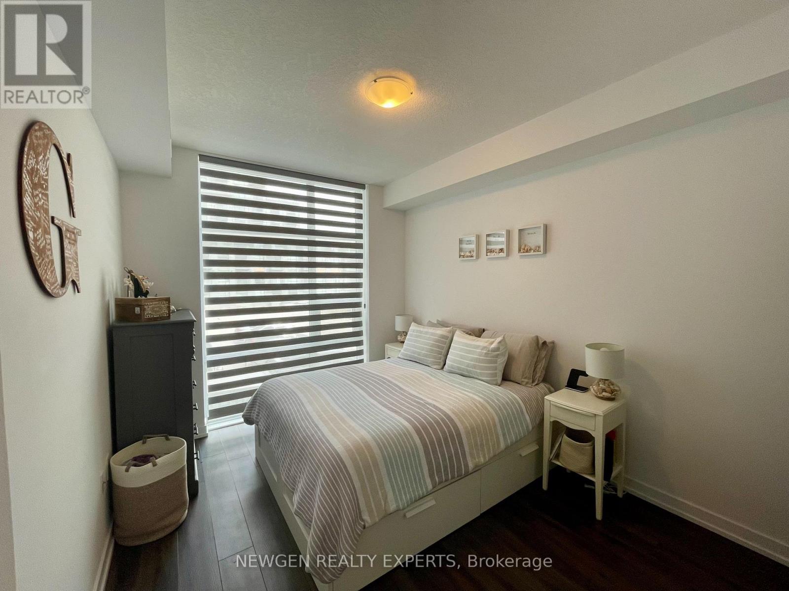 A bedroom with a bed, nightstand, and window with blinds.