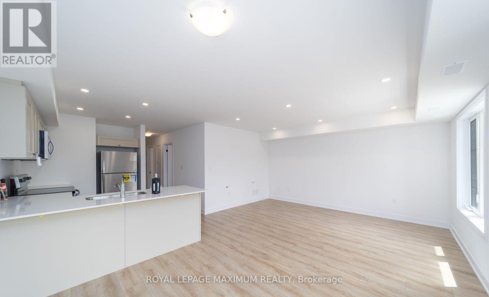 A spacious room with wooden flooring and white walls, featuring a kitchen area with stainless steel appliances.
