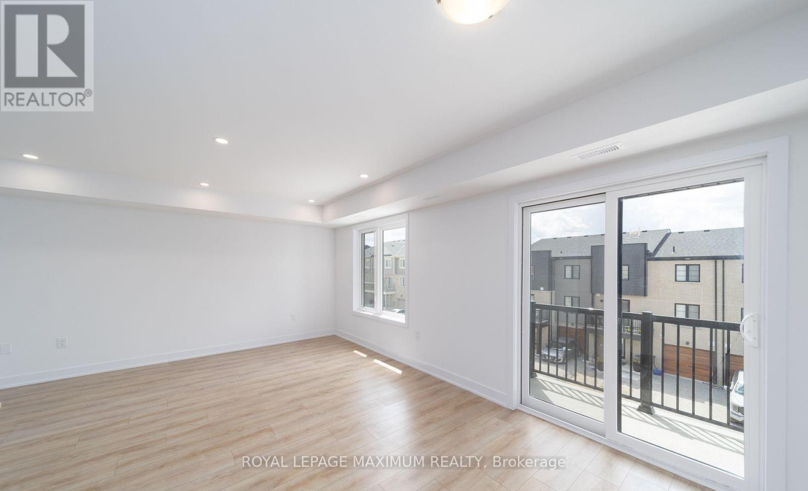 A spacious room with wooden flooring and a sliding glass door leading to a balcony.
