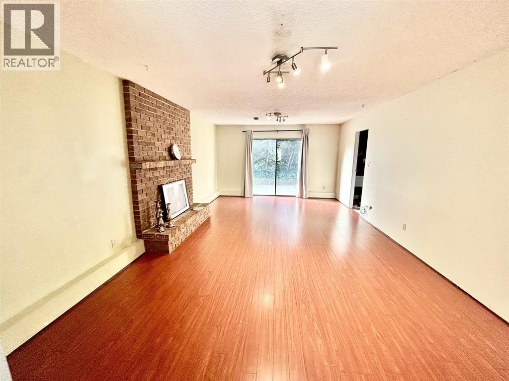 A large empty room with wooden floors and a brick fireplace.