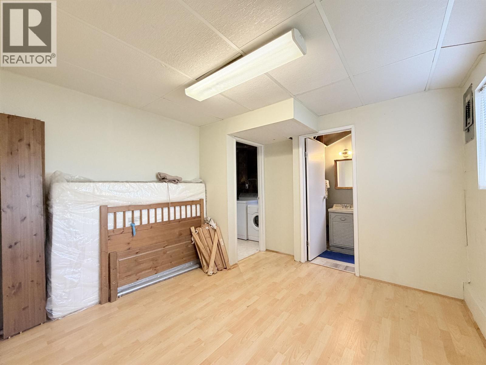 A bedroom with a bed, dresser, and a washing machine in the other room.