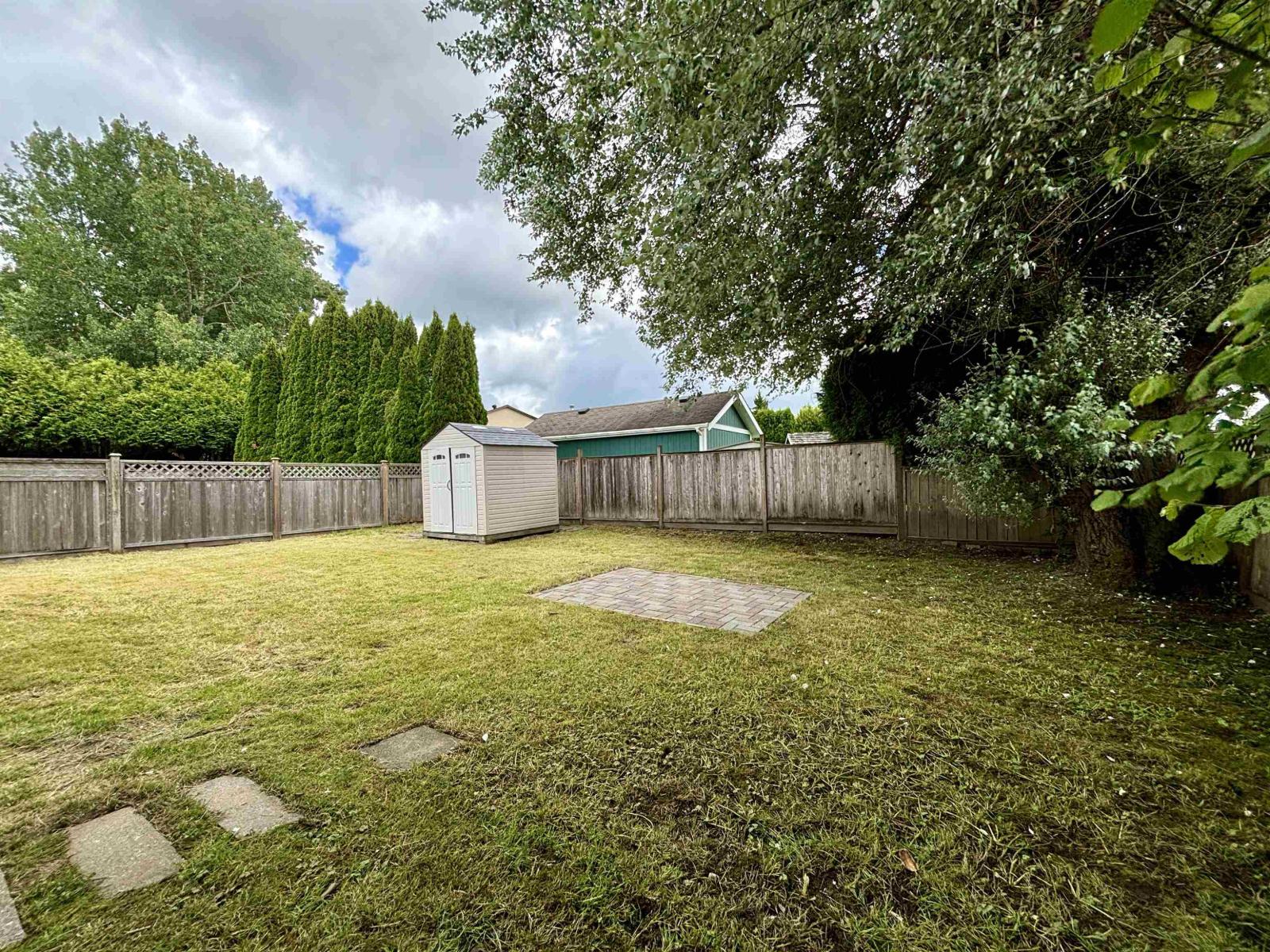 A backyard with a fence, a shed, and a tree.