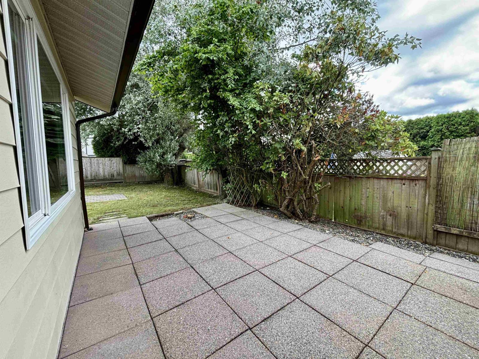 A backyard with a paved patio and a fence.