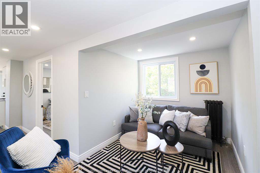 A living room with a black and white striped rug, a blue armchair, a black sofa, and a painting on the wall.