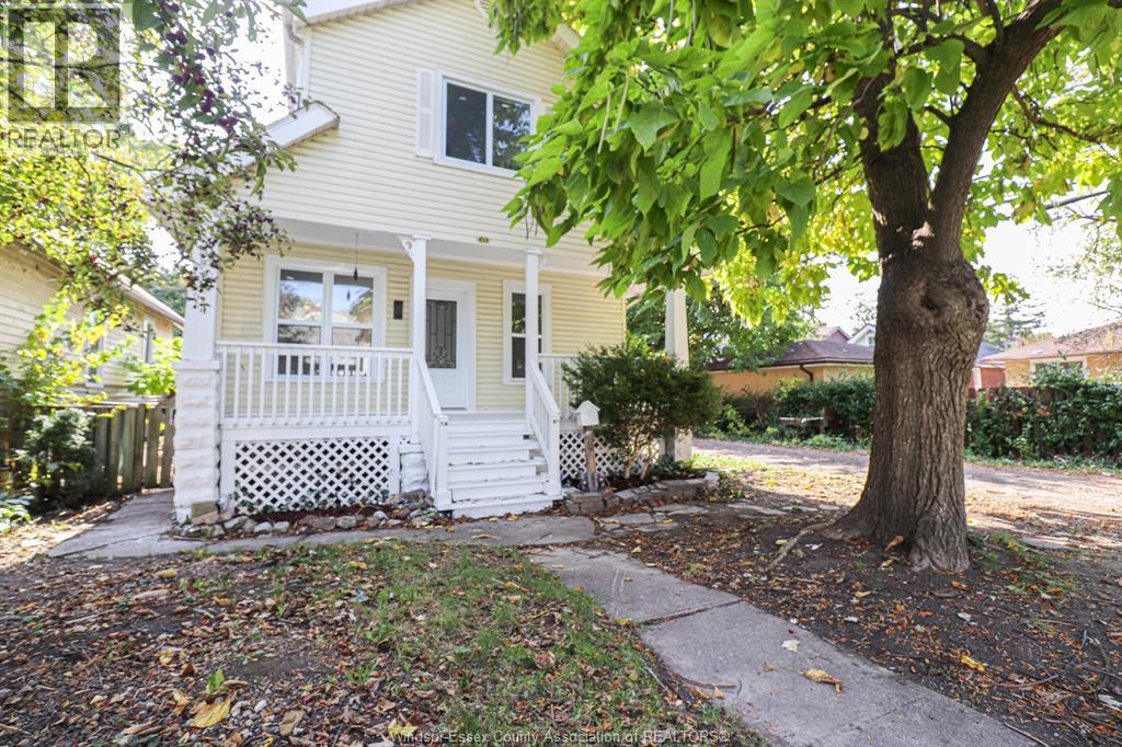 A yellow house with a white porch and a tree in front.
