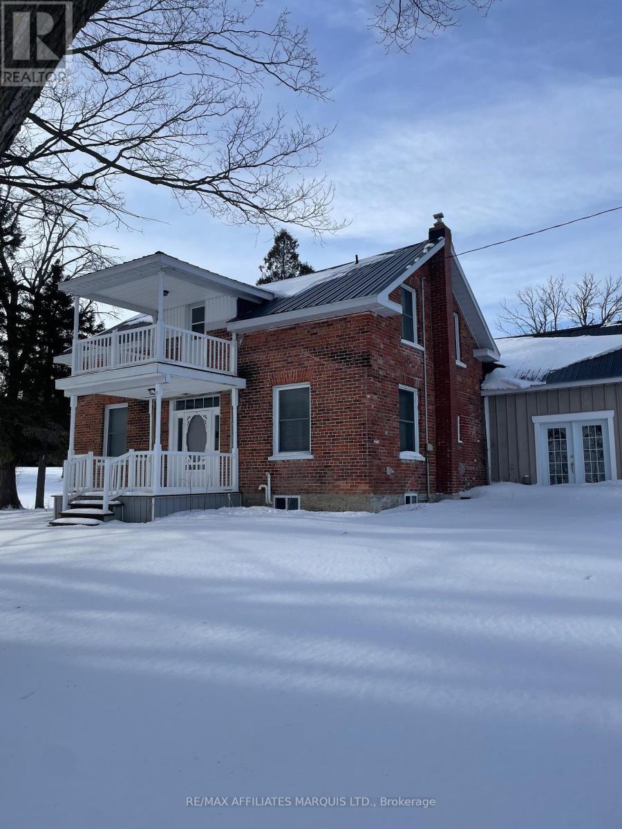 A house with a red brick chimney and a white porch is surrounded by snow.