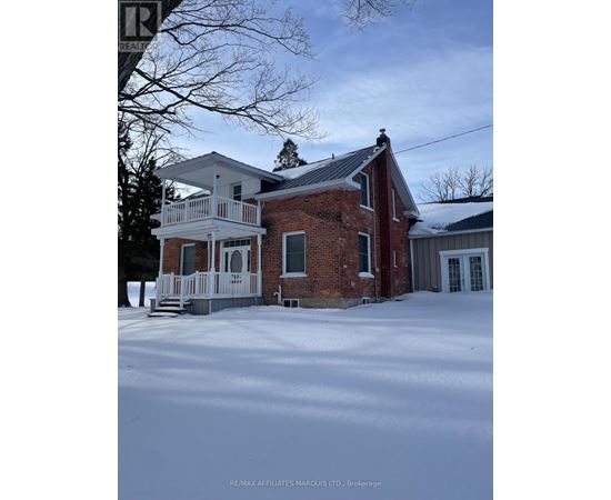 A house with a red brick chimney and a white porch is surrounded by snow.