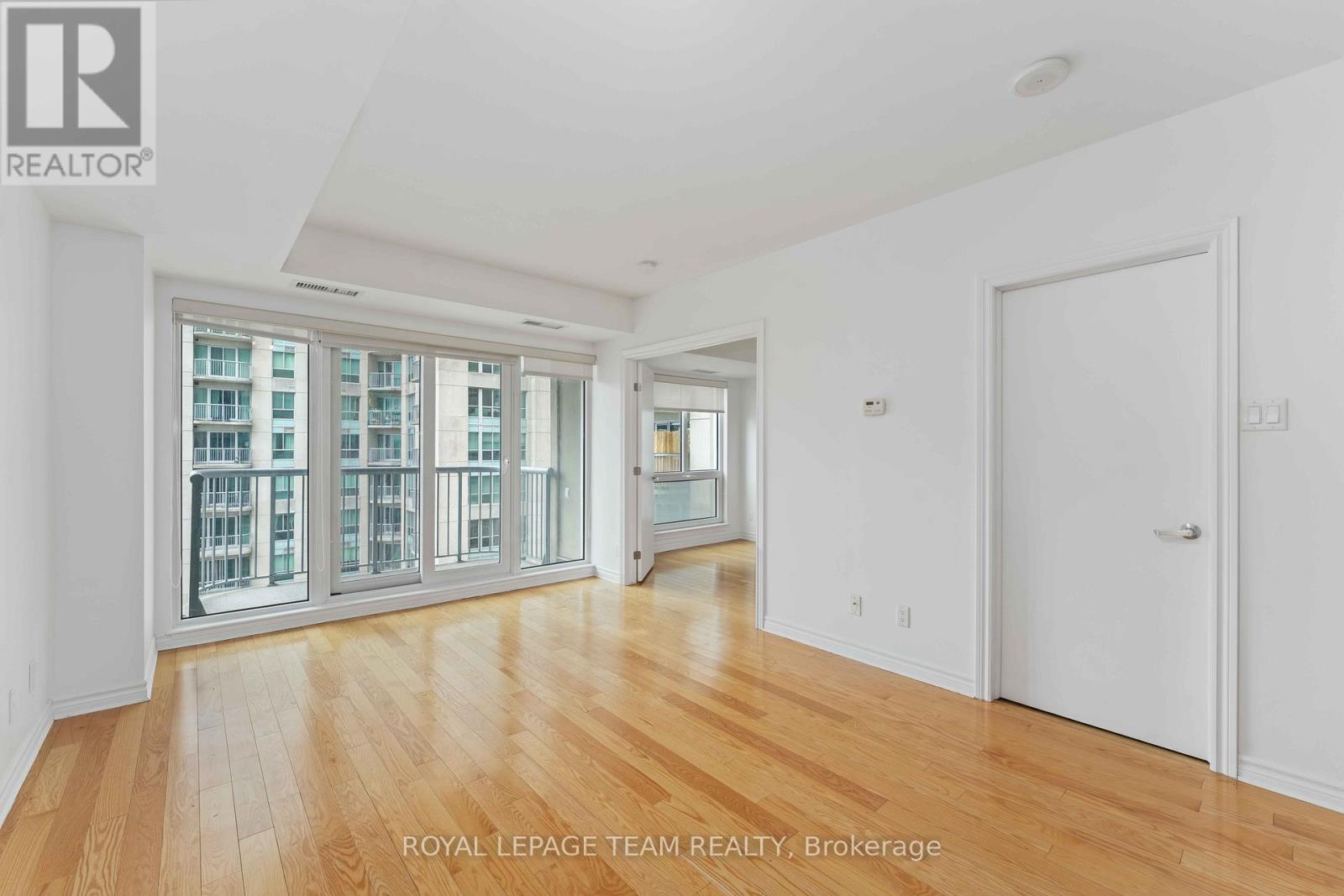 A spacious room with wooden floors and a large window with a view of a building outside.