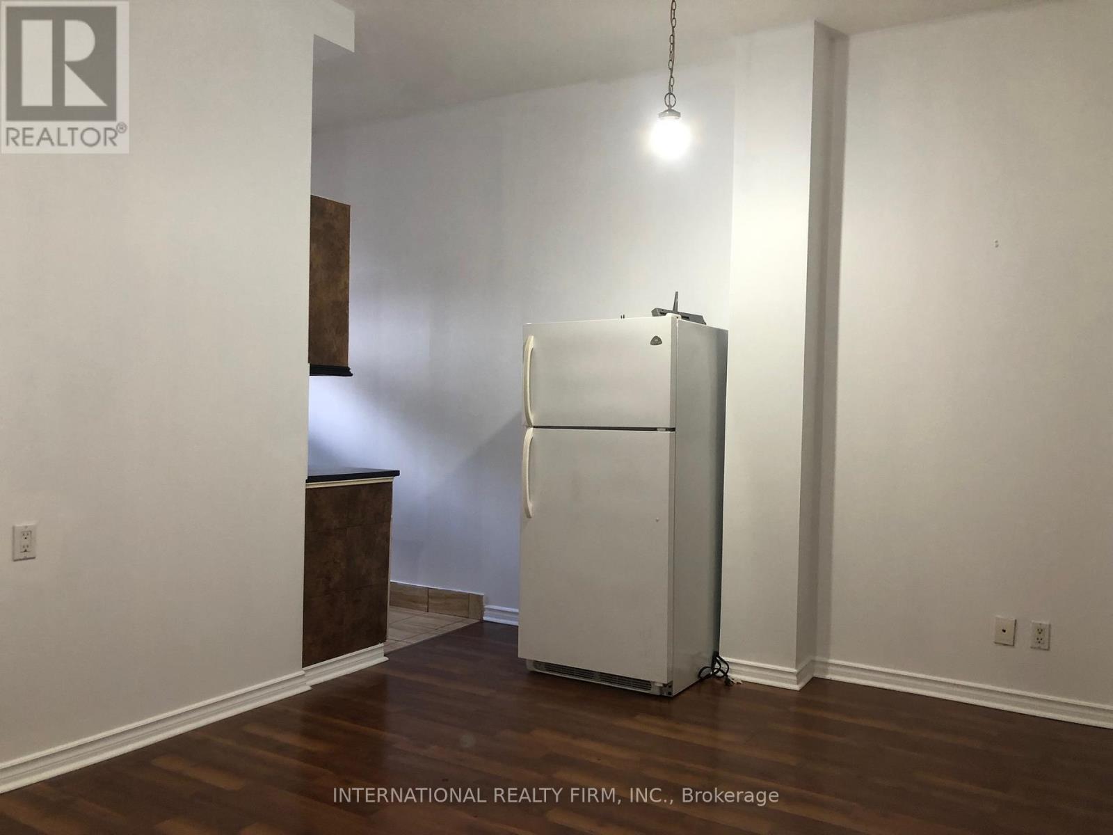 A white refrigerator in a room with wood flooring and white walls.