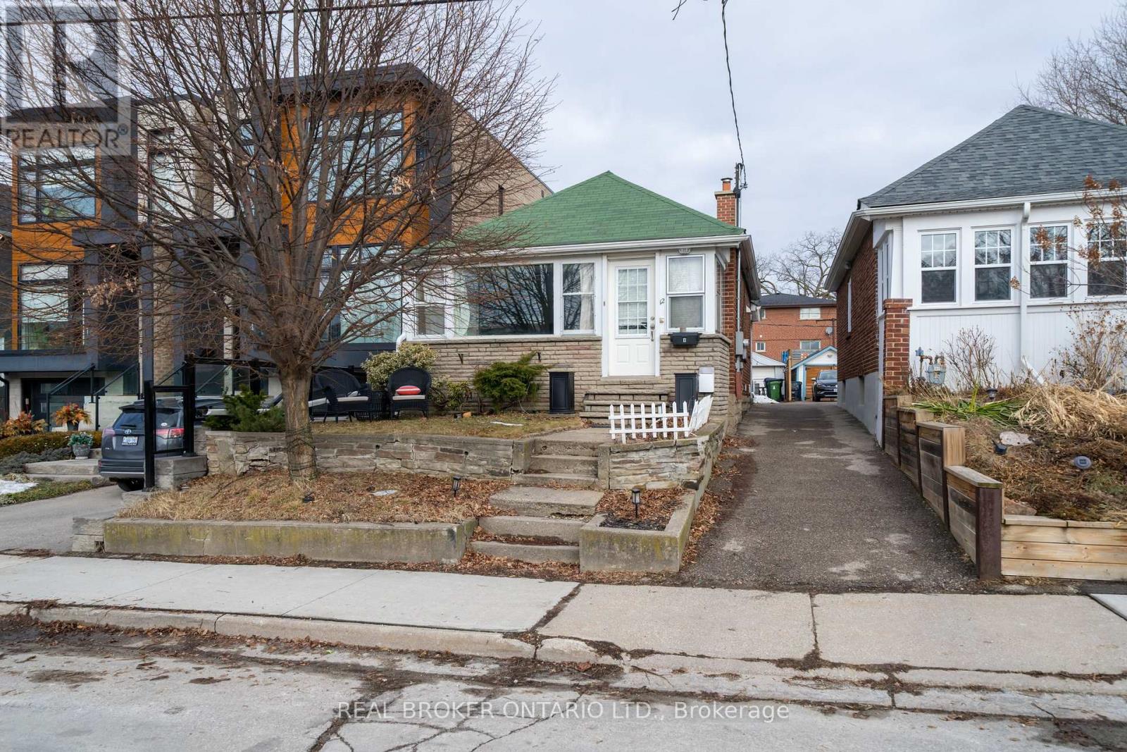 A residential street with a house on the right and a tree in front of a house on the left.