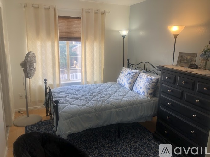 A bedroom with a bed, dresser, and window with curtains.
