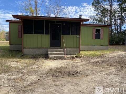 A green house with a black door and windows is surrounded by a dirt field.