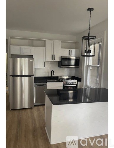 A kitchen with a refrigerator, microwave, oven, and a hanging light fixture.