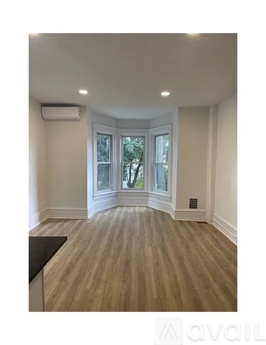 A room with wooden flooring and a window overlooking a tree.